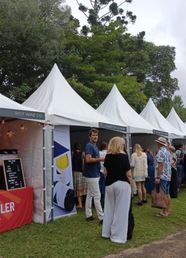 White tents with people, one tent with a sign that reads "RIOT WINE CO."