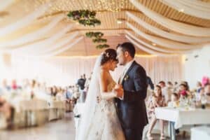 Bride and groom embracing during their first dance at a wedding reception with draped fabric ceilings and fairy lights.