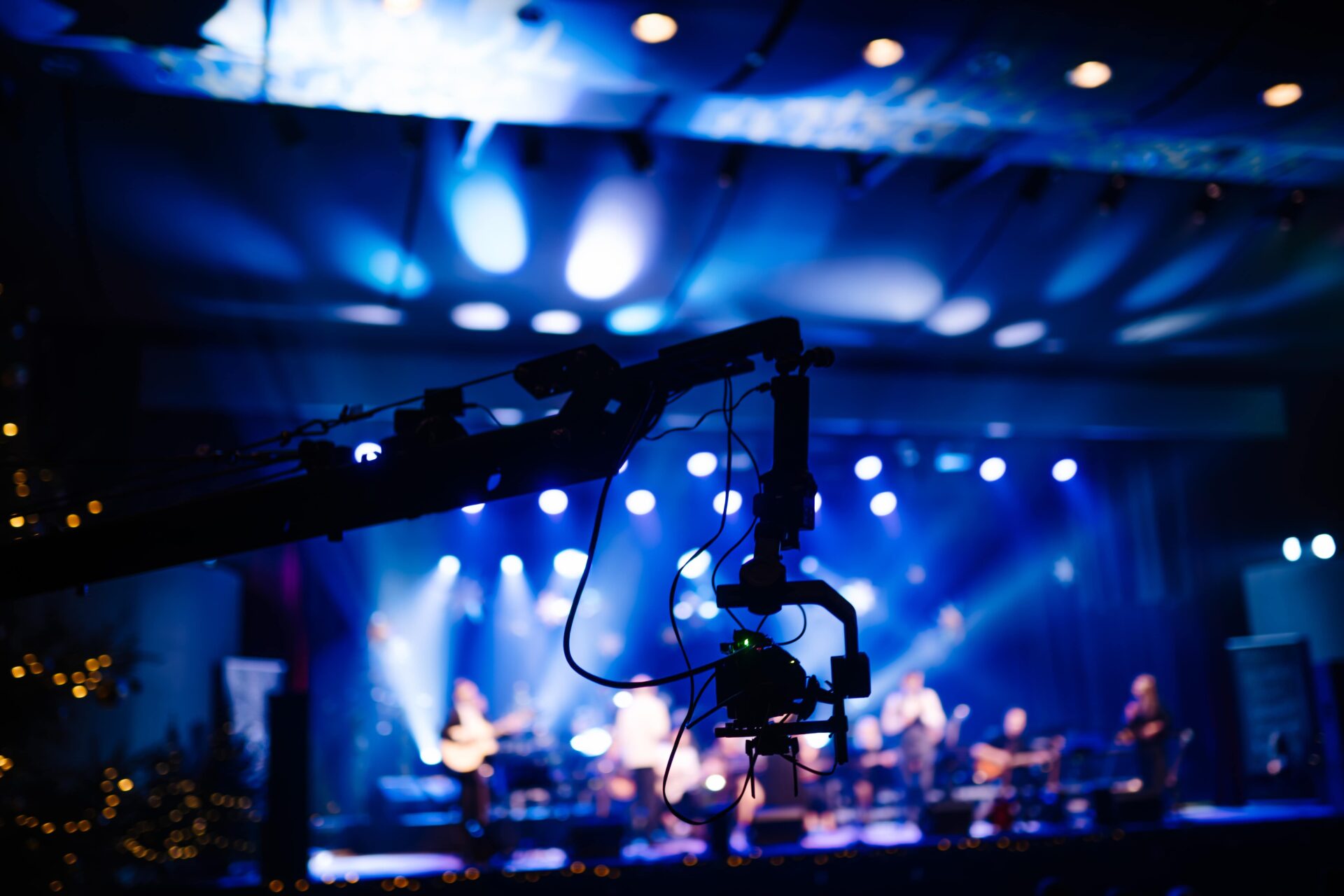 Camera crane or jib arm overlooking a stage bathed in bright blue and white lights during a concert or live performance.