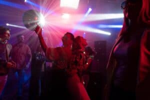 People dancing under bright red and blue lights from a spinning disco ball at a nightclub party.