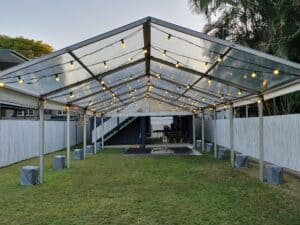 A clear pavilion tent with fairy lights set up on a grassy area.