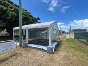 A white marquee tent with clear walls, set up outdoors near a sign that reads "NO PARKING ACCESS ONLY EMERGENCY VEHICLE."