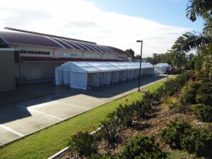 A long white tent set up in a parking lot next to a building.