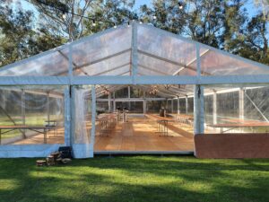 A clear marquee tent with wooden tables and string lights