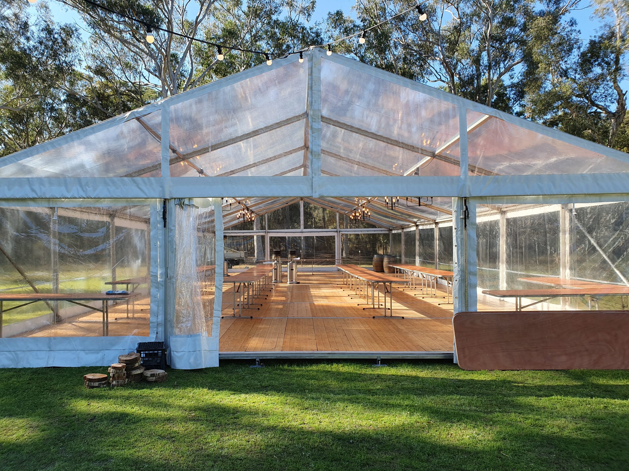 A clear marquee tent with wooden tables and string lights