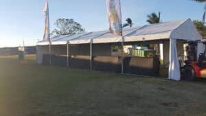 Exterior view of a white event marquee tent with black lower walls and advertising flags set up on a grassy field.