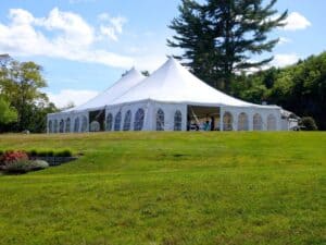 Large white twin-pole event tent or marquee set up on a grassy lawn under a blue sky.